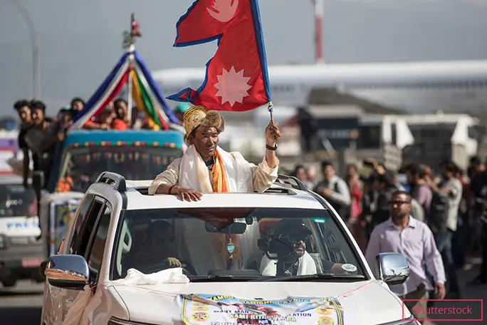 24回目のエベレスト登頂を終え、ネパールの首都でネパールの国旗を掲げるカミ・リタ