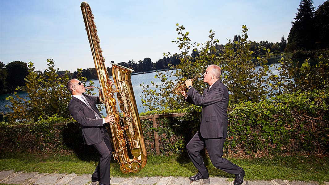 a man playing the largest saxophone next to a man playing the regular-sized one