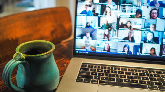 blue mug next to laptop with several faces on a video call