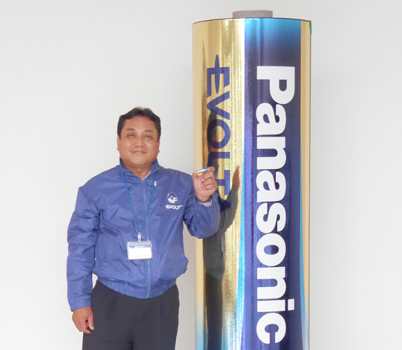 man standing next to huge panasonic battery